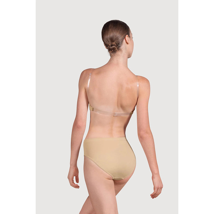 A model shown from the back wearing a beige high-waisted shapewear brief and a clear back-support bra against a light gray studio background.