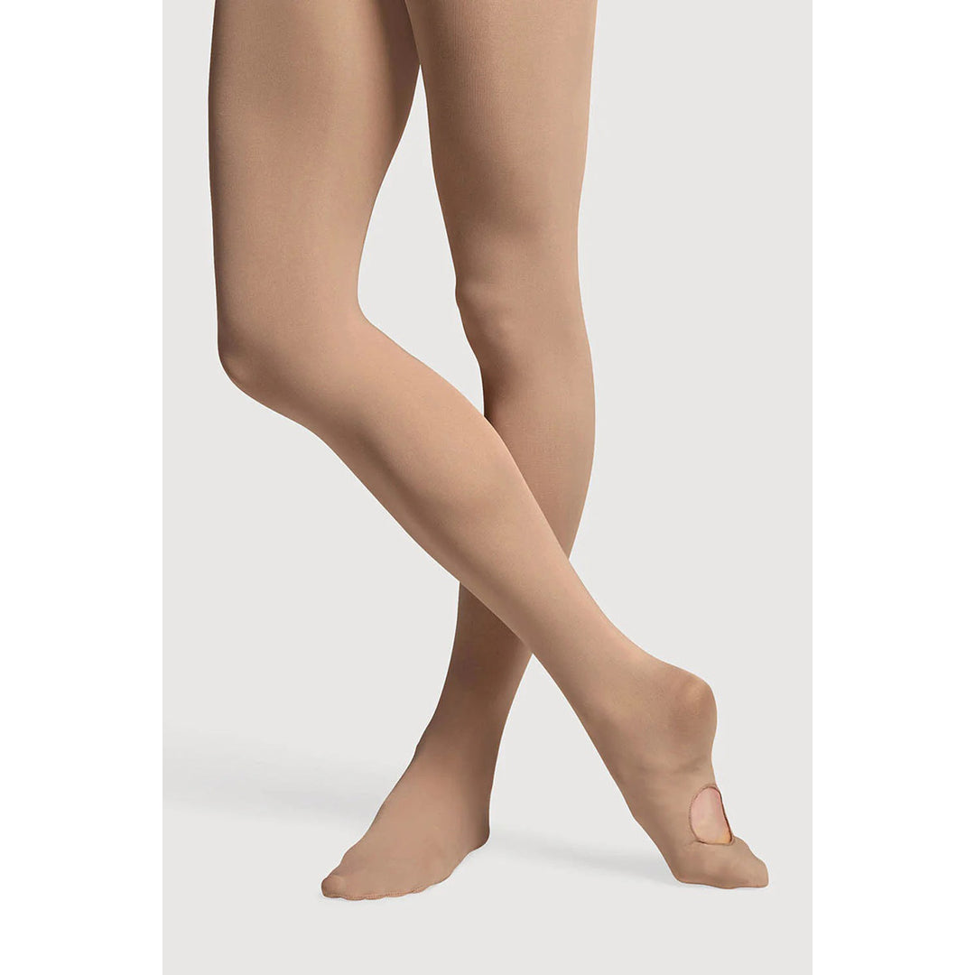 Close-up of a person's legs wearing sheer nude/tan tights with a small oval cutout on the sole of one foot, shown against a light gray studio background.