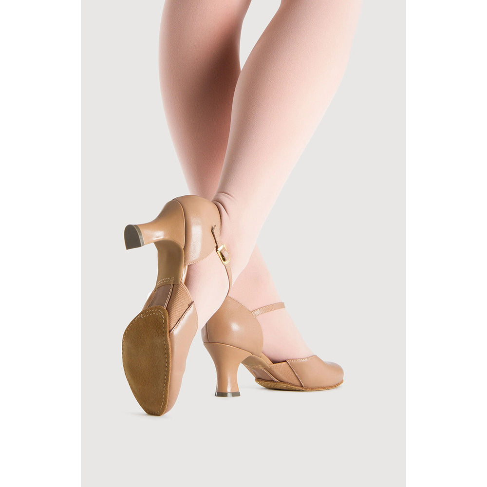 A pair of women's tan dance shoes with ankle straps and kitten heels, shown on a model wearing light pink tights against a light gray background.