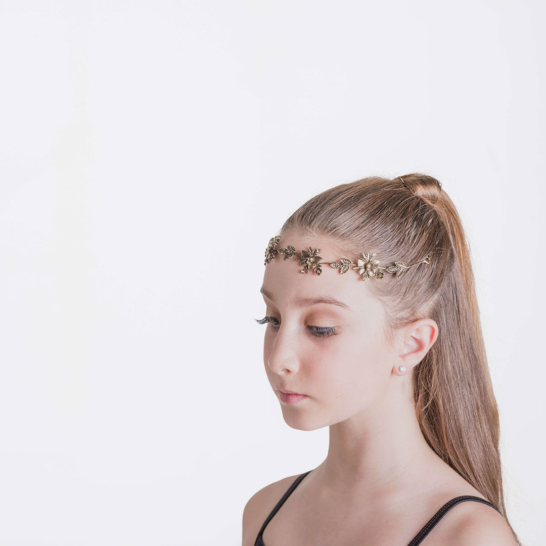 Girl with her hair in a high ponytail wearing a gold hairpiece of flowers and leaves across her forehead