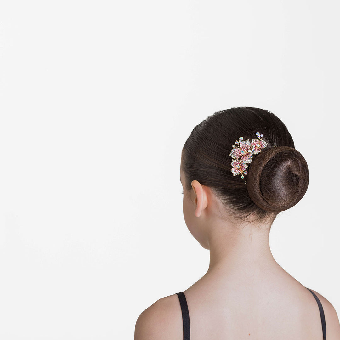 Small floral hair comb with clear and pink crystals sitting beside a ballet bun