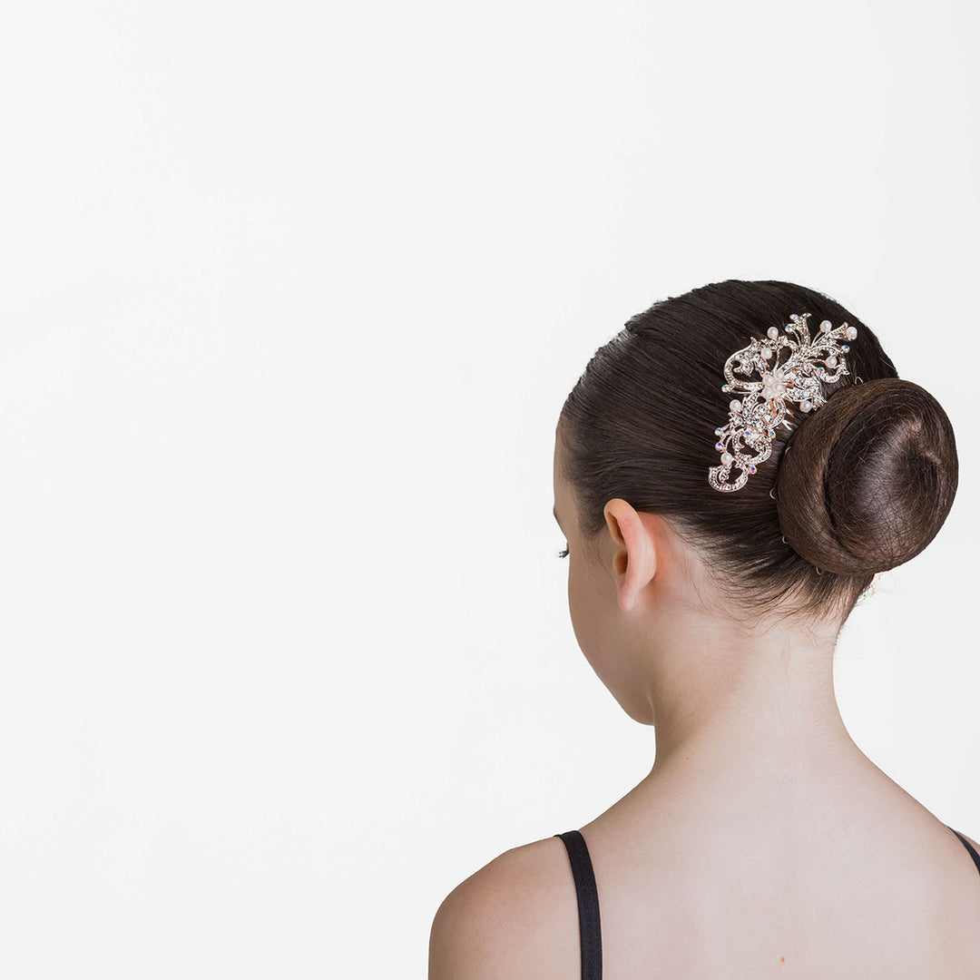 Rose gold hair comb with sparkle and pearl detail sitting beside a ballet bun